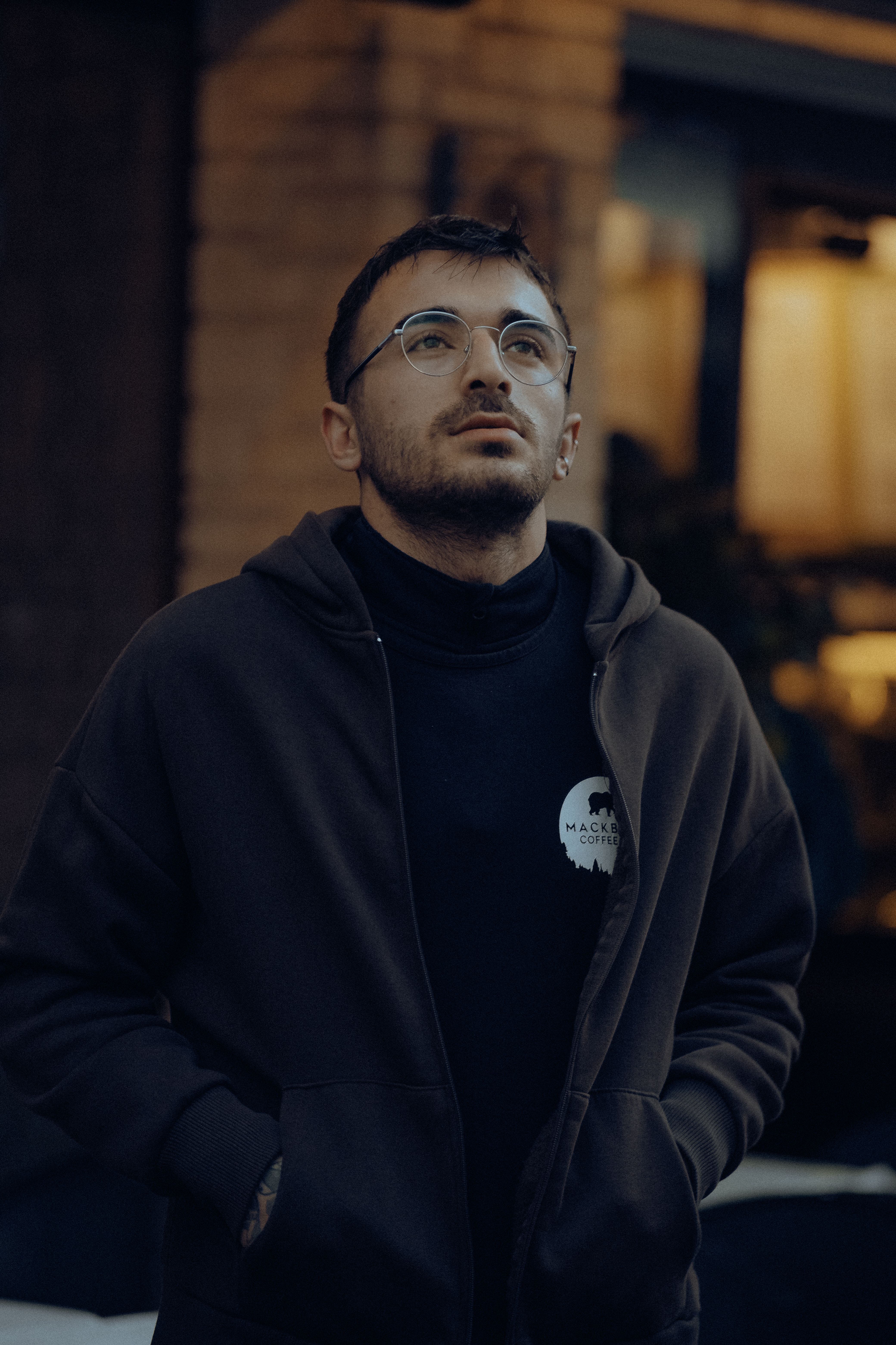 A man in a hoodie looks upwards in an urban setting, exuding a contemplative mood.