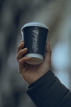 A close-up shot of a hand holding a disposable coffee cup outdoors with blurred background.