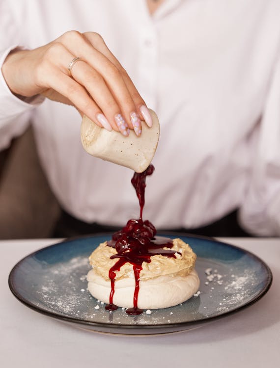 Person's Hand Pouring Fruit Jam over a Meringue