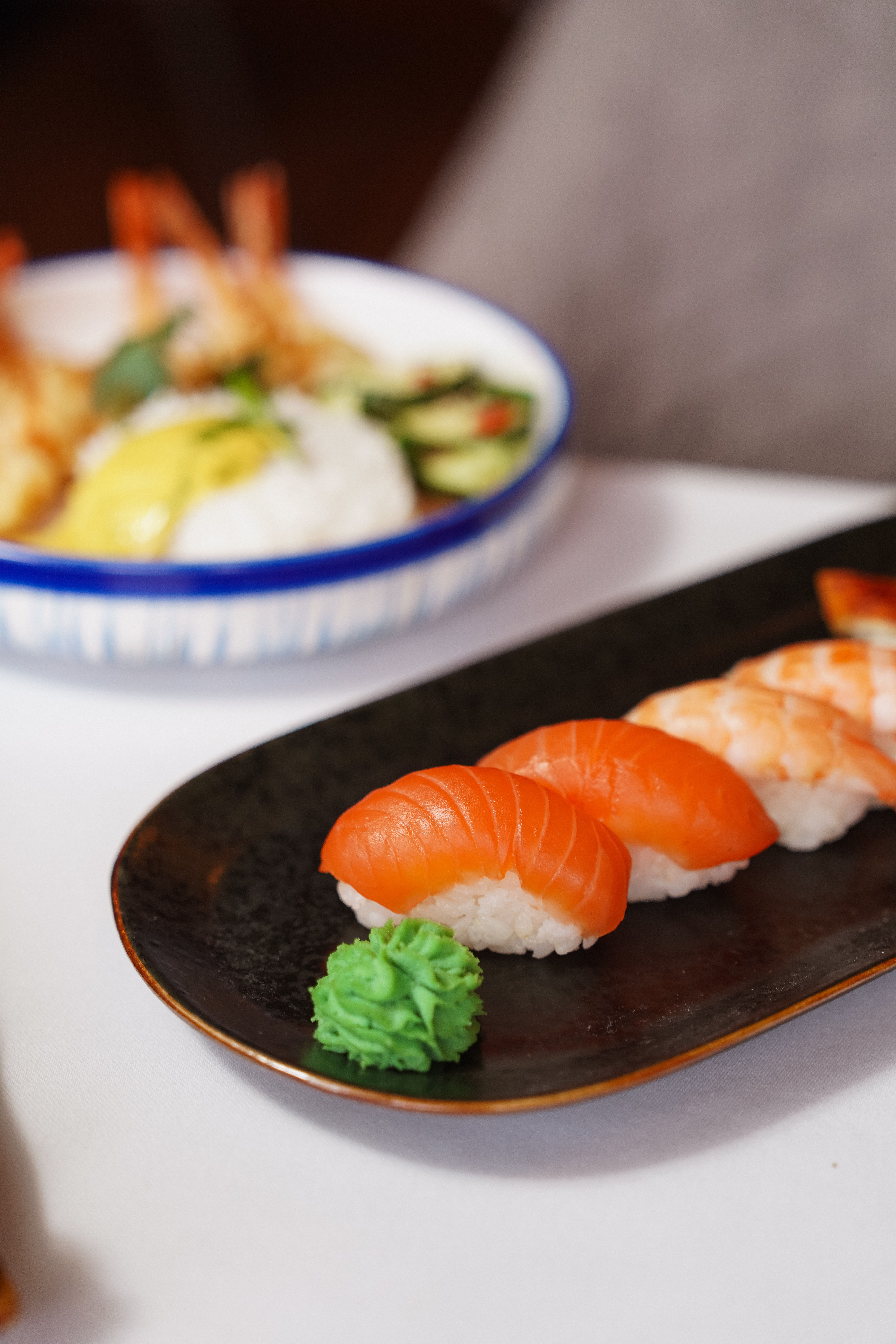 Six pieces of nigiri sushi on a dark wooden board, hand-pressed rice topped with tuna, salmon, shrimp, and tamago, with pickled ginger and a small dish of soy sauce alongside
