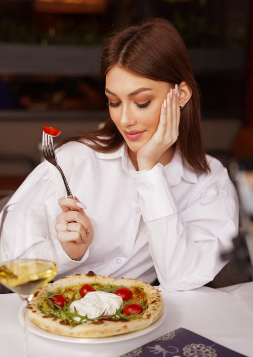 Young Woman with a Cherry Tomato on a Fork Looking at the Pizza Plate