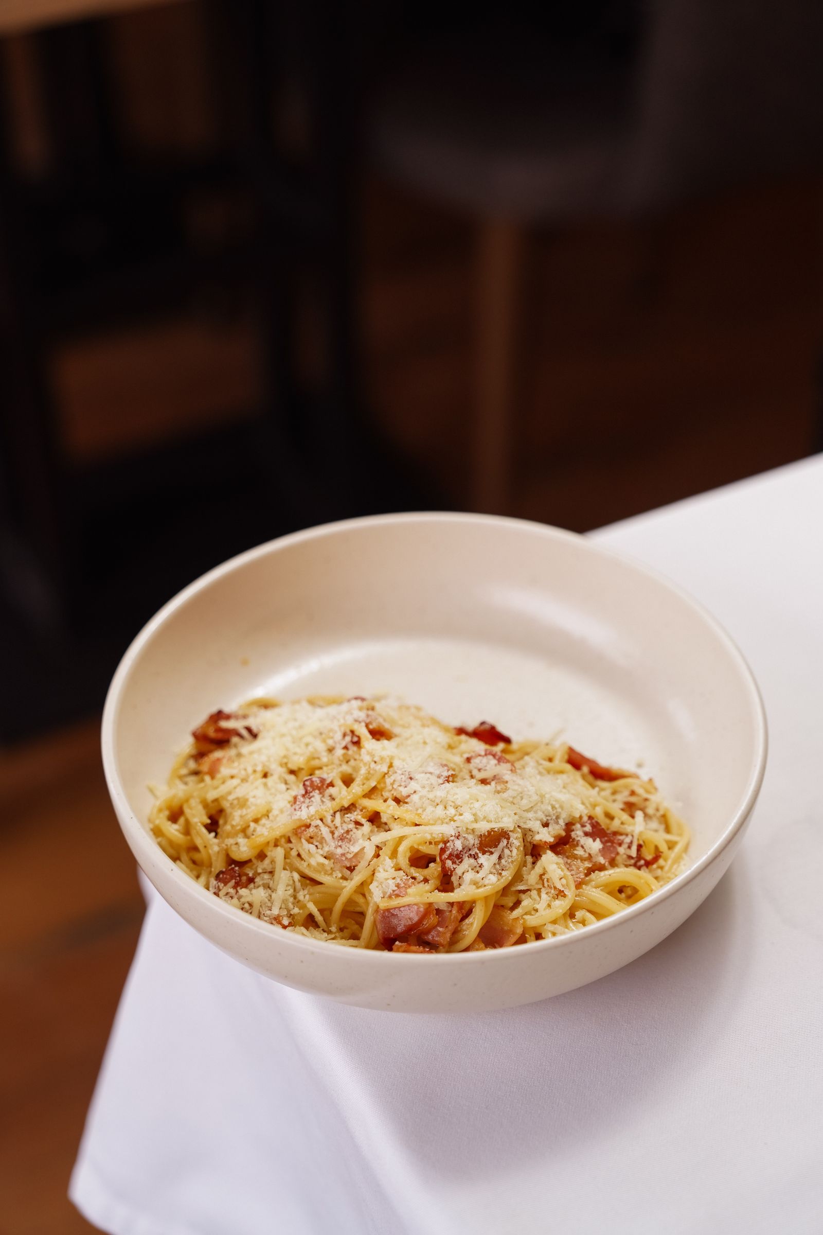 A plate of creamy carbonara-style pasta with parmesan on a rustic table