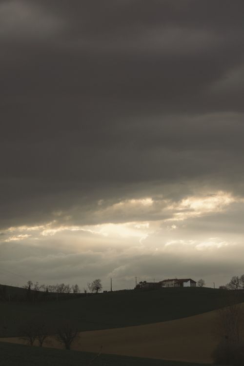 Free A dramatic overcast sky with sunlight breaking through over a rural landscape and distant village. Stock Photo