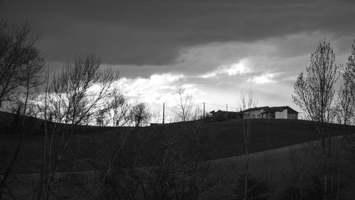 Free Peaceful rural landscape with house on hill under a cloudy sky, captured in black and white. Stock Photo
