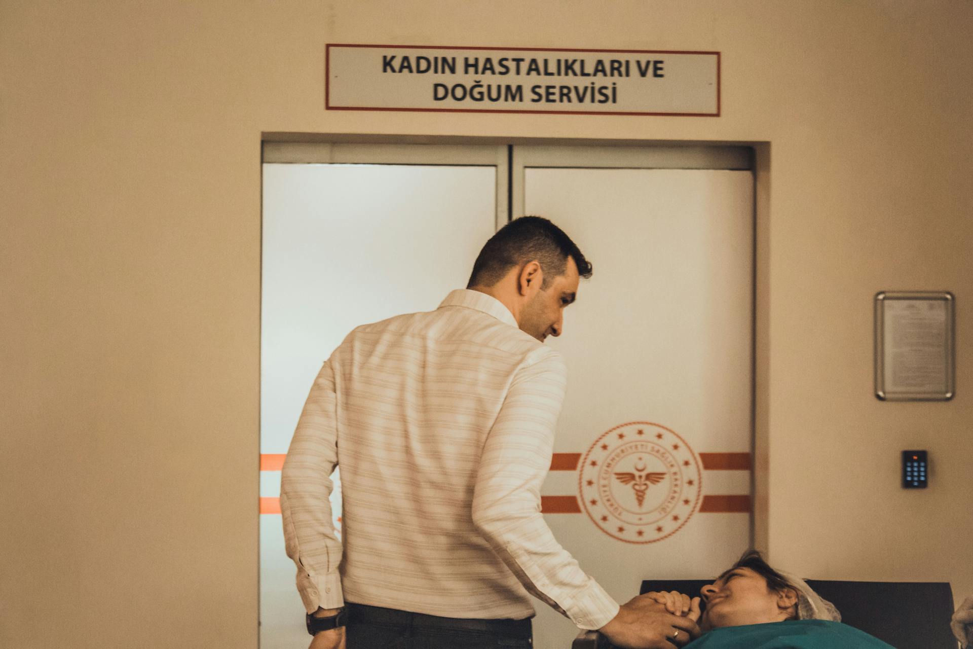 A man supports a woman in the maternity ward of a hospital, holding hands.