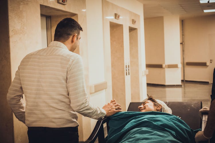 Man Comforting Stressed Woman On Bed In Hospital