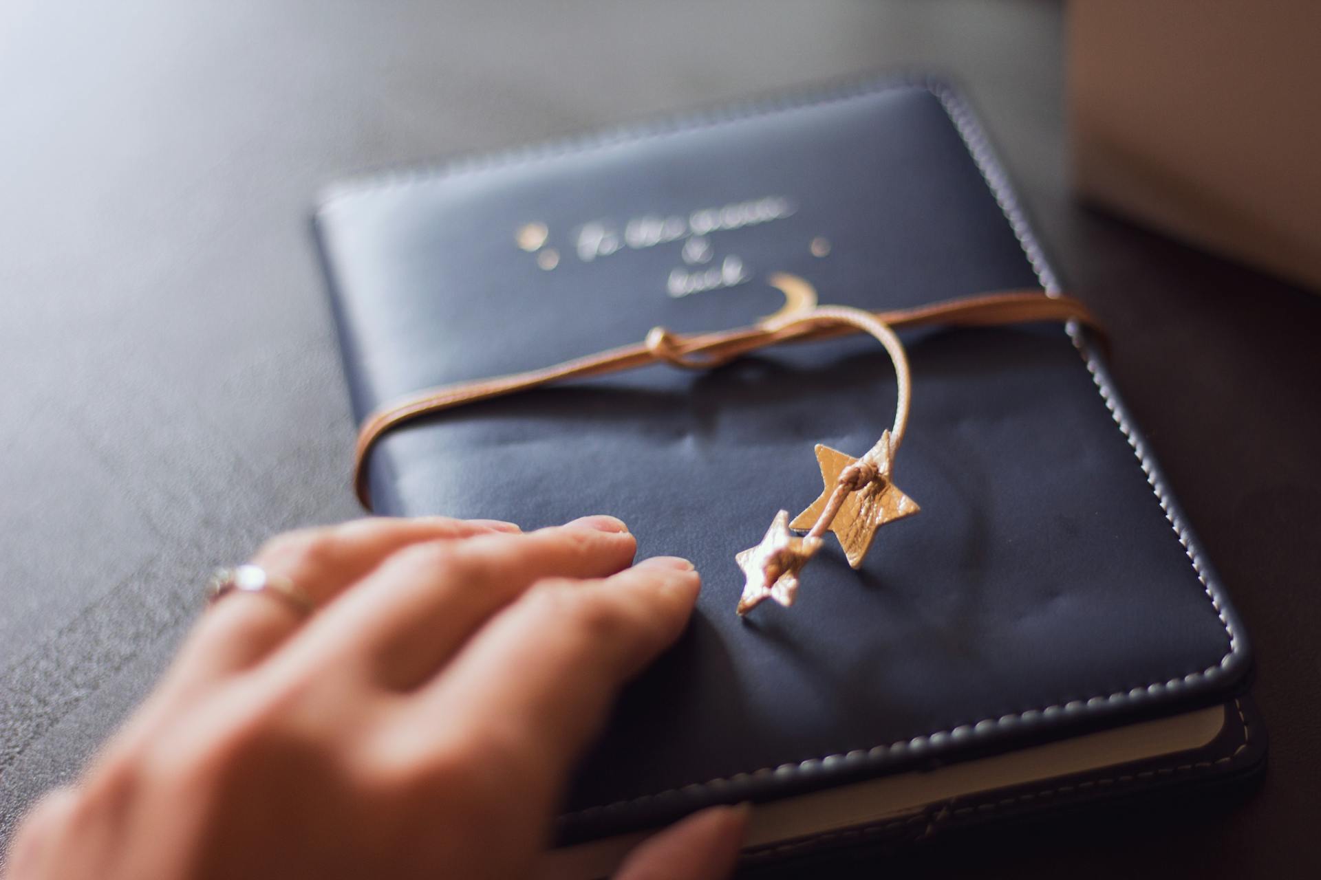 Close-up of a hand touching a stylish leather journal with a star charm, conveying a sense of elegance and reflection.