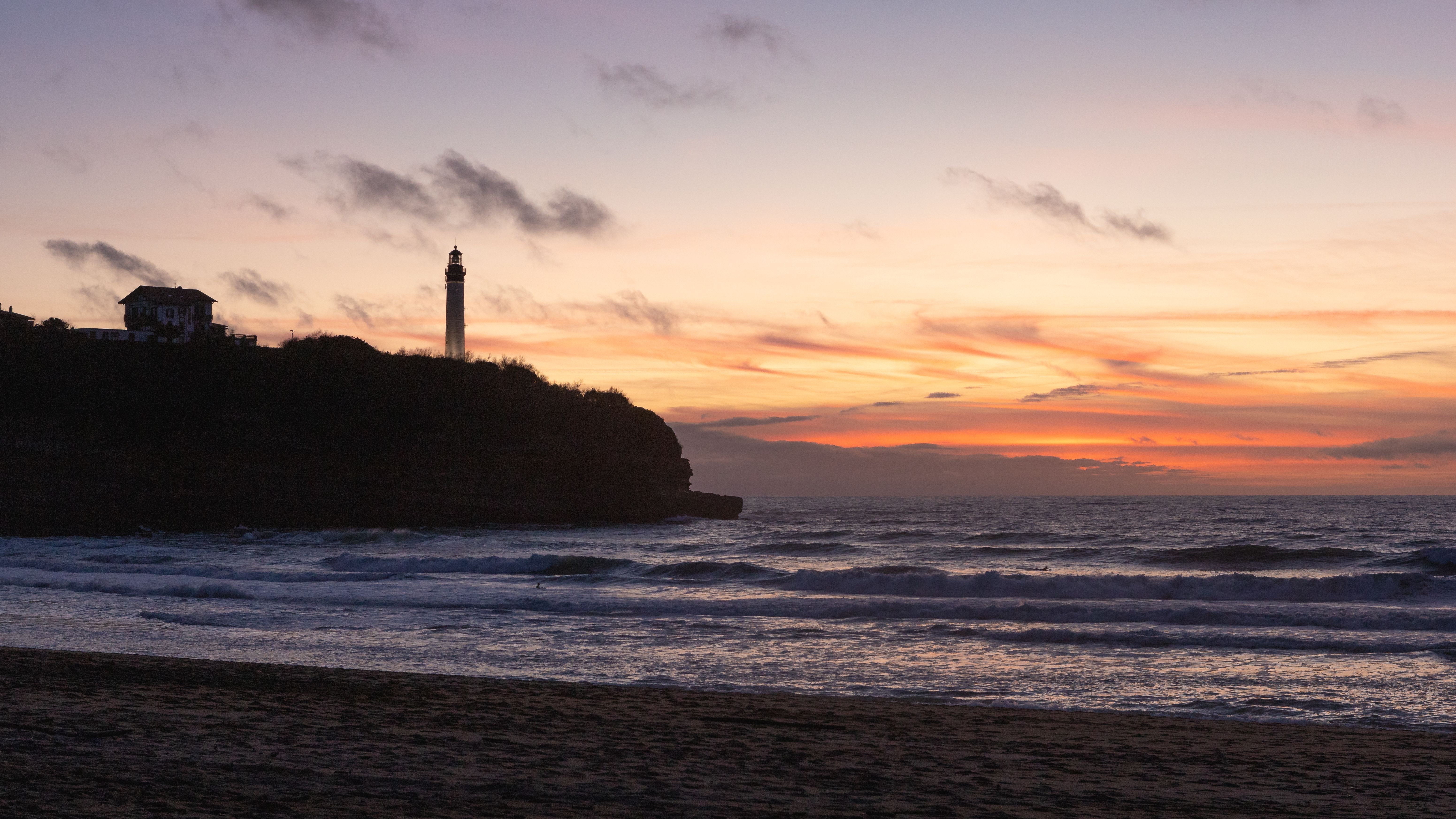 A breathtaking sunset over the ocean with a lighthouse silhouette, perfect for serene beach themes.
