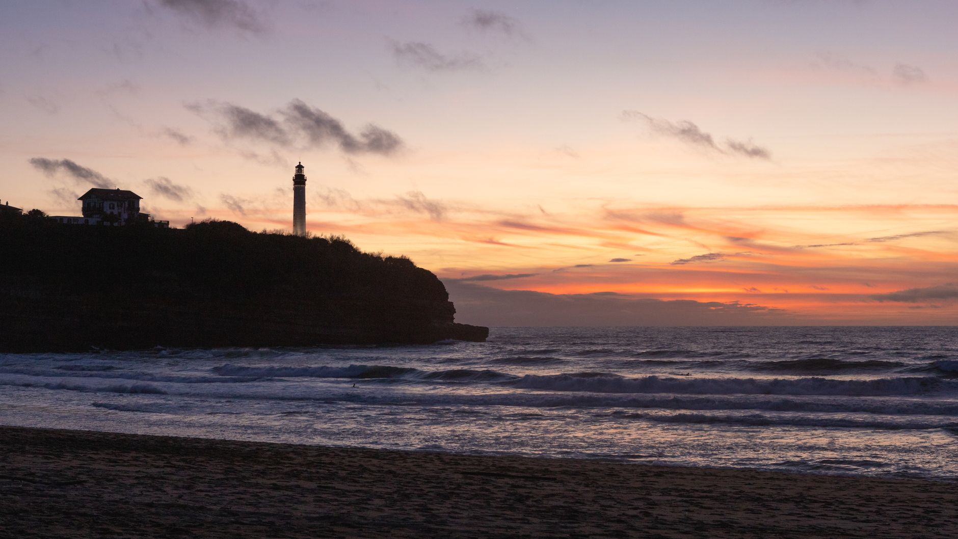 A breathtaking sunset over the ocean with a lighthouse silhouette, perfect for serene beach themes.