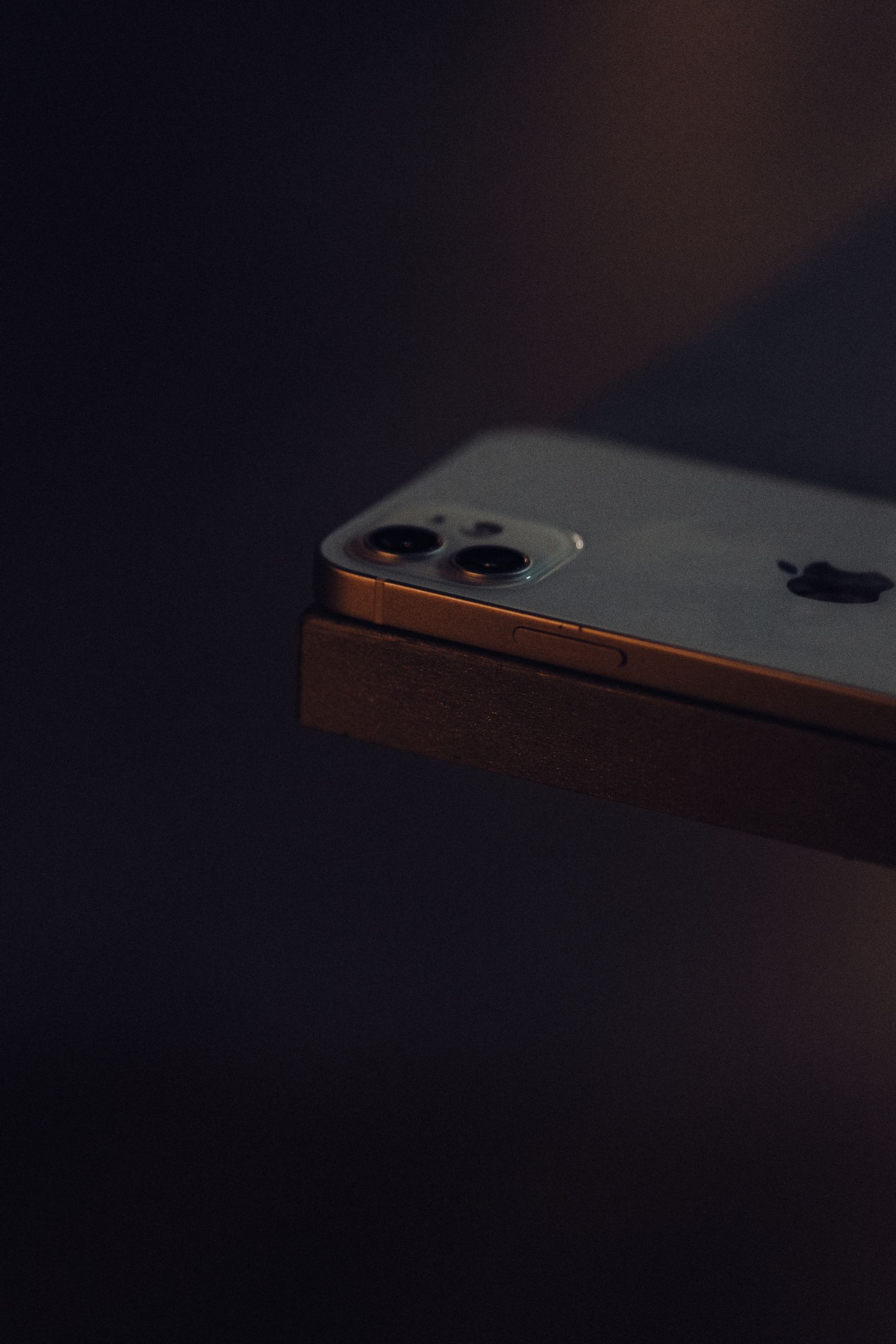A smartphone with a dual camera lens resting on a surface in low light