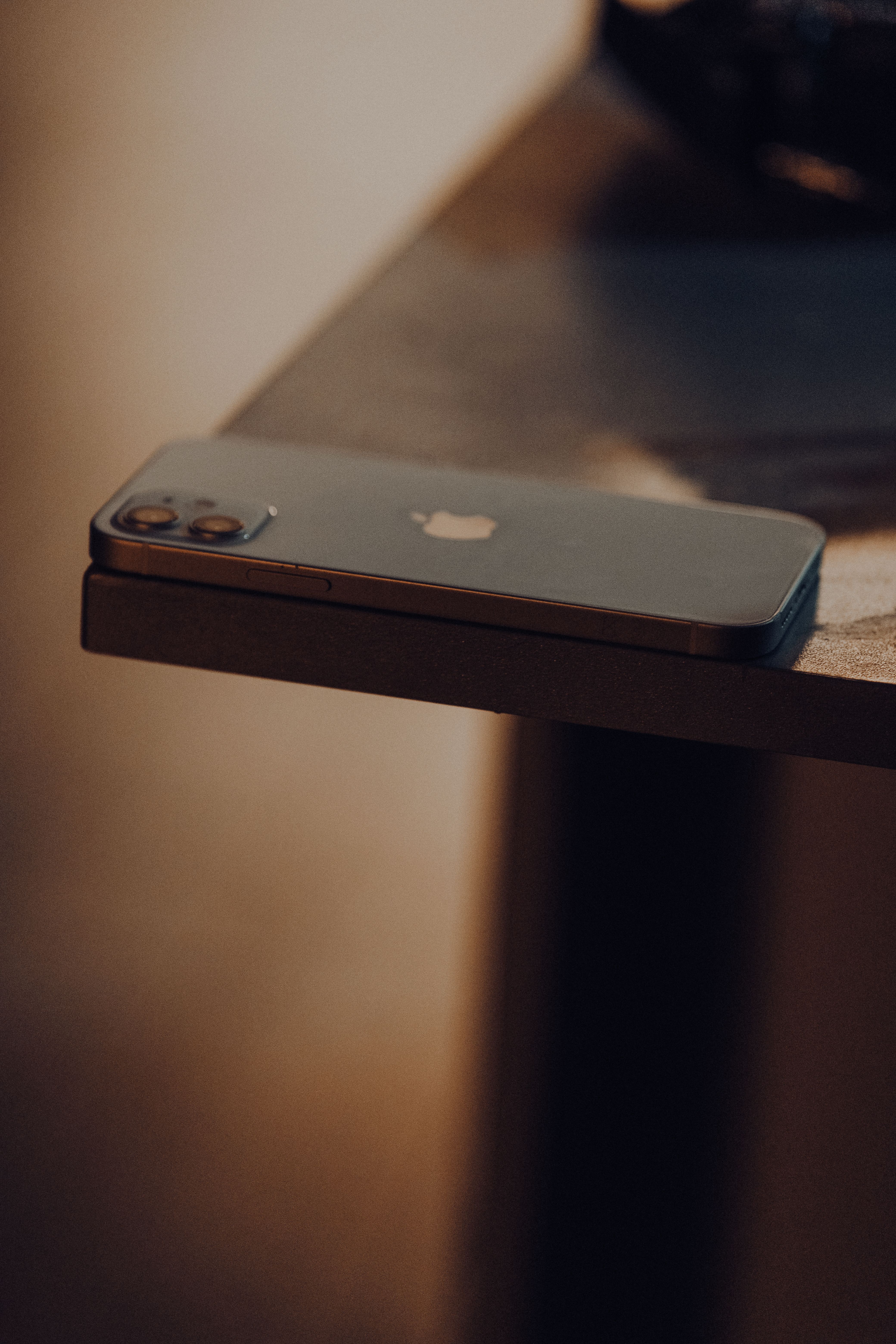 A phone lying face down on the edge of a dark wooden table in low evening light