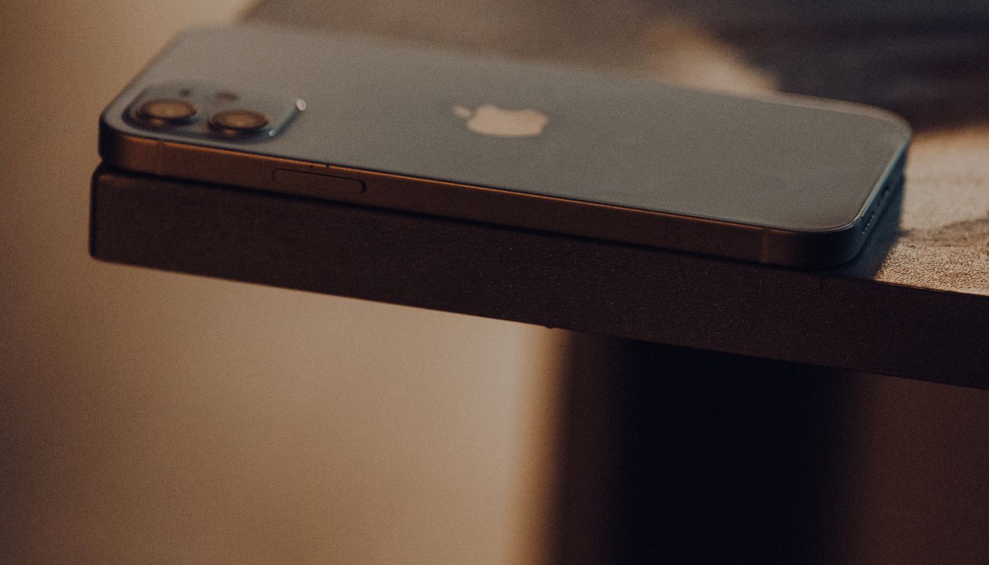 A phone lying face down on the edge of a dark wooden table in low evening light