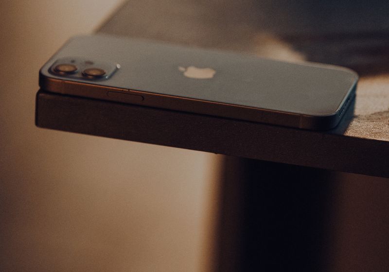 A phone lying face down on the edge of a dark wooden table in low evening light