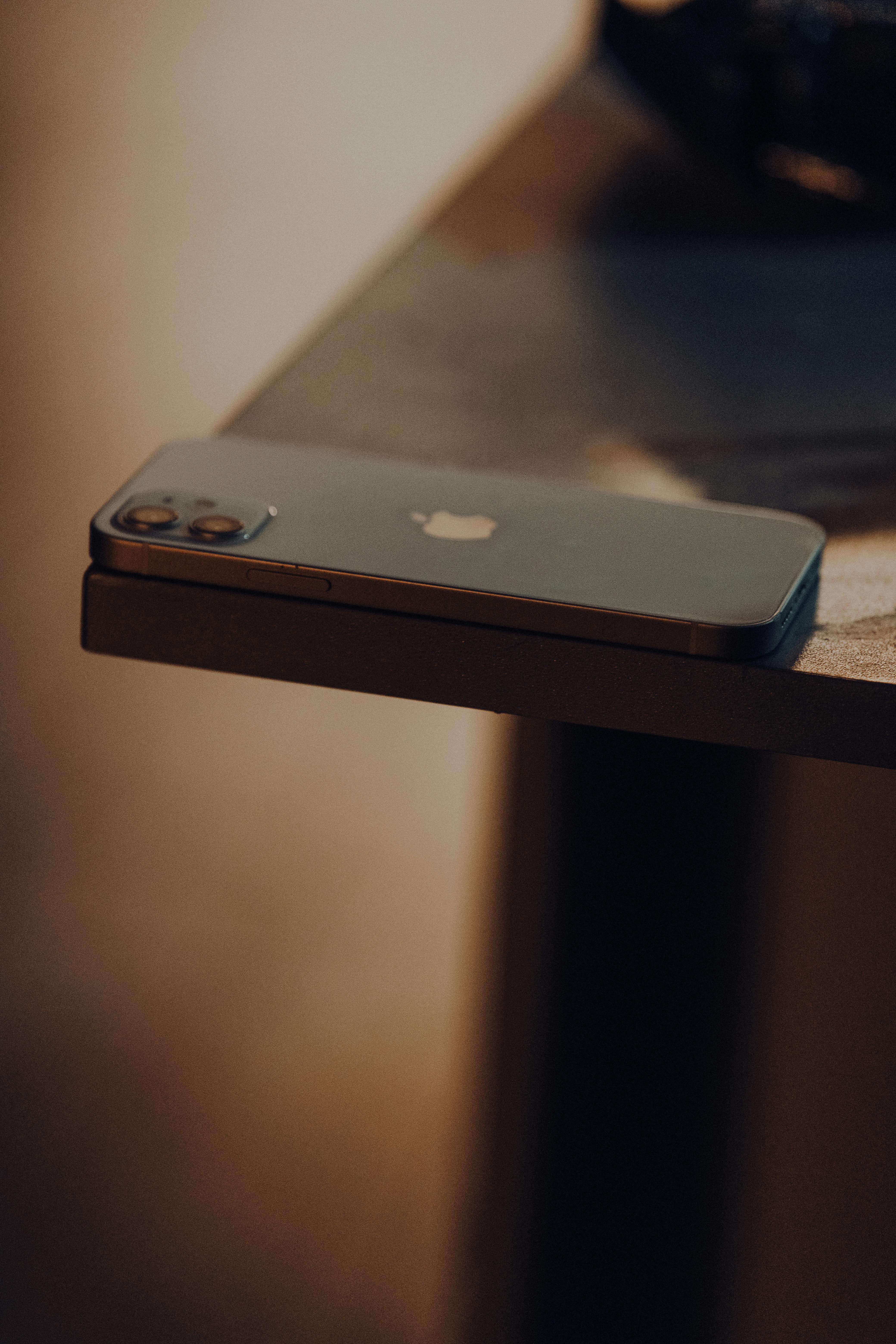 Free Close-up of a modern smartphone placed on the edge of a wooden table, highlighting minimalist design. Stock Photo