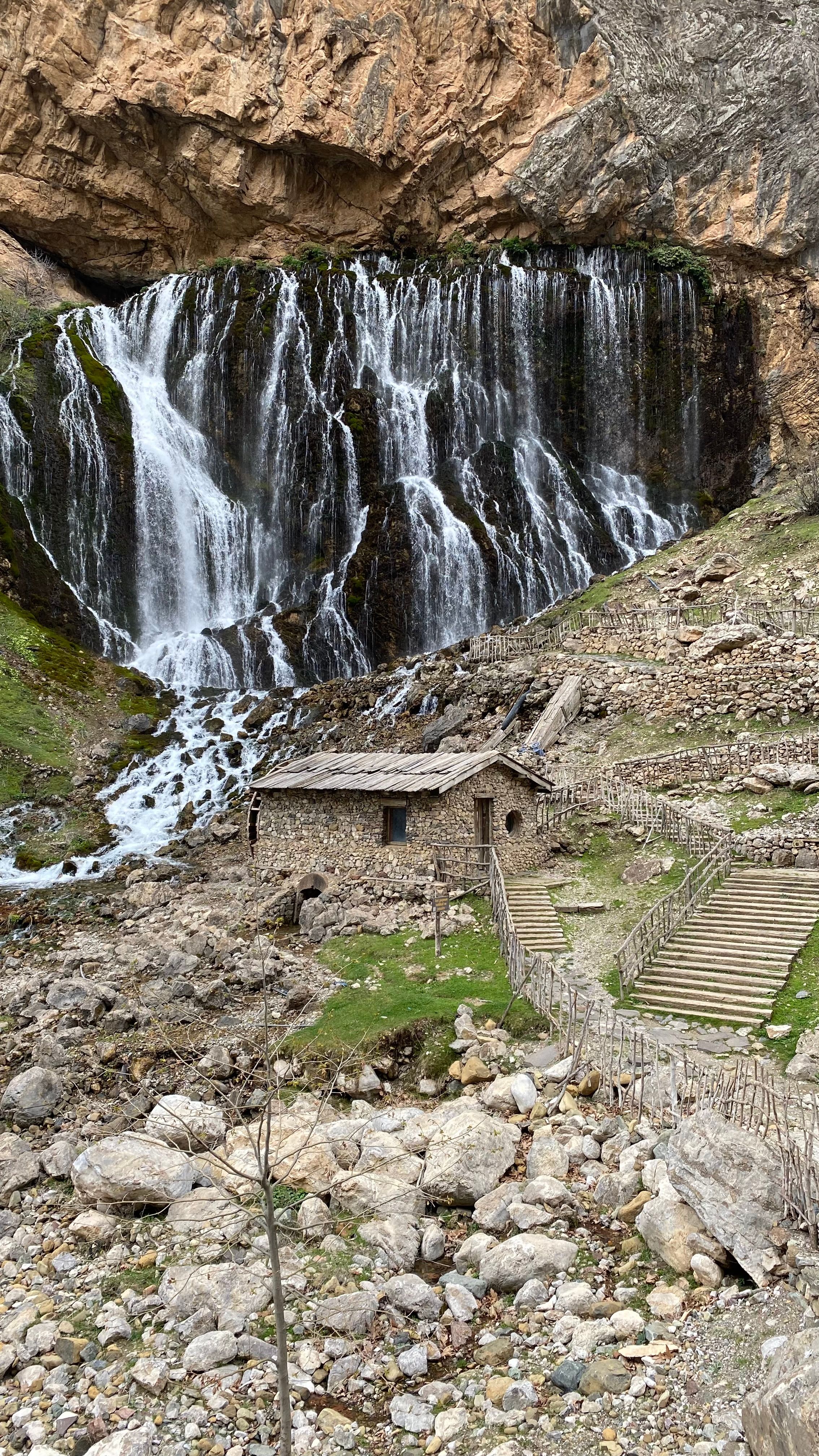 Captivating view of Kapuzbaşı waterfall cascading beside rustic stone house in Türkiye.