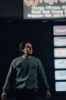 Fashionable young man in casual sportswear standing under neon signs at night.