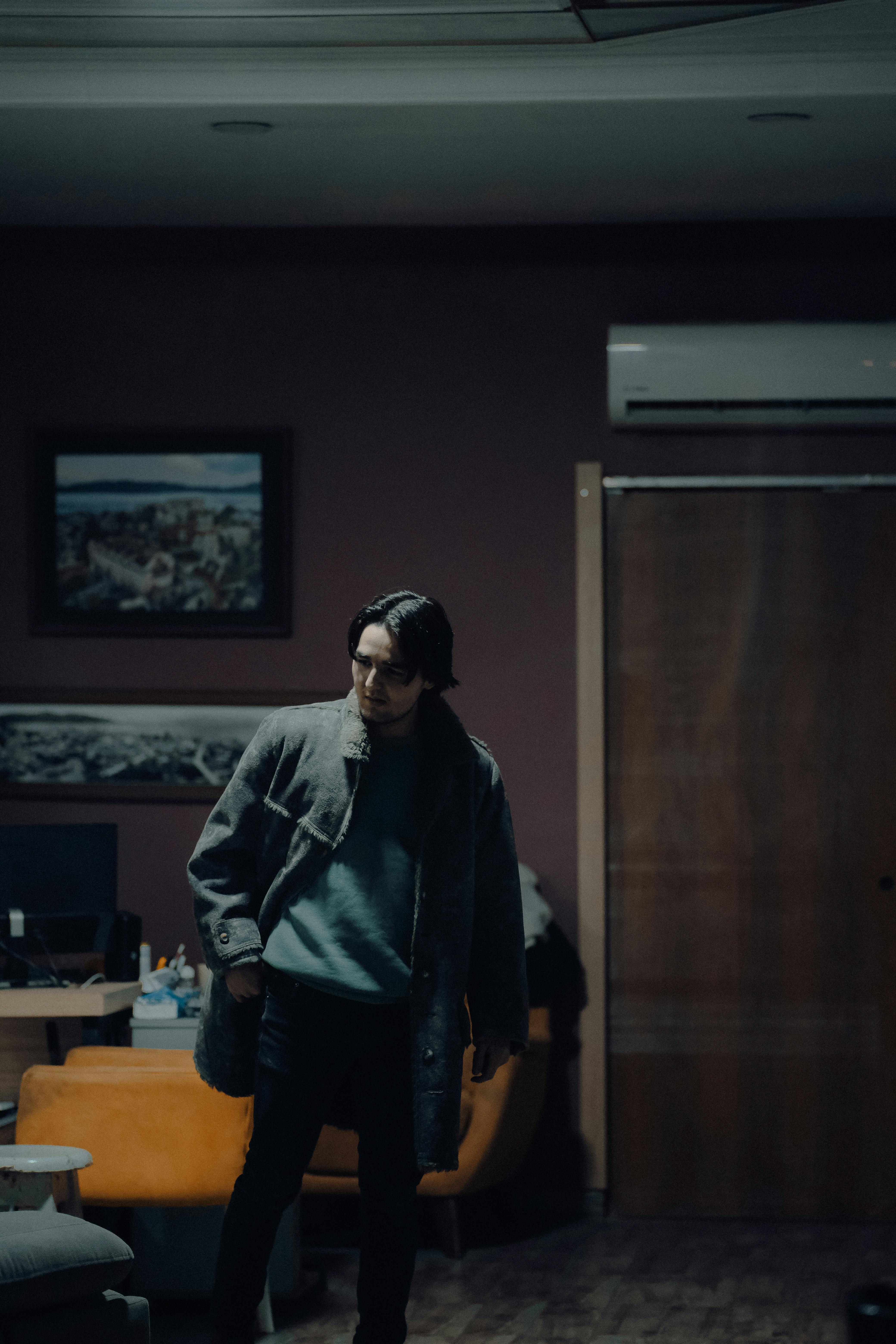 Stylish portrait of a man in a coat posing indoors with moody lighting.