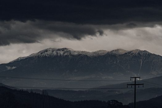 Snowcapped mountain range under a dramatic, stormy sky with dark clouds and moody atmosphere.