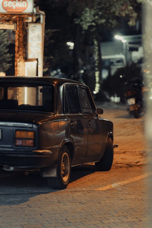 Free A vintage car parked on a dimly lit city street at night, capturing a nostalgic vibe. Stock Photo