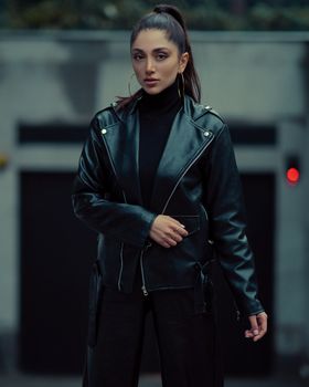 Fashionable woman in leather jacket posing outdoors with confident look.