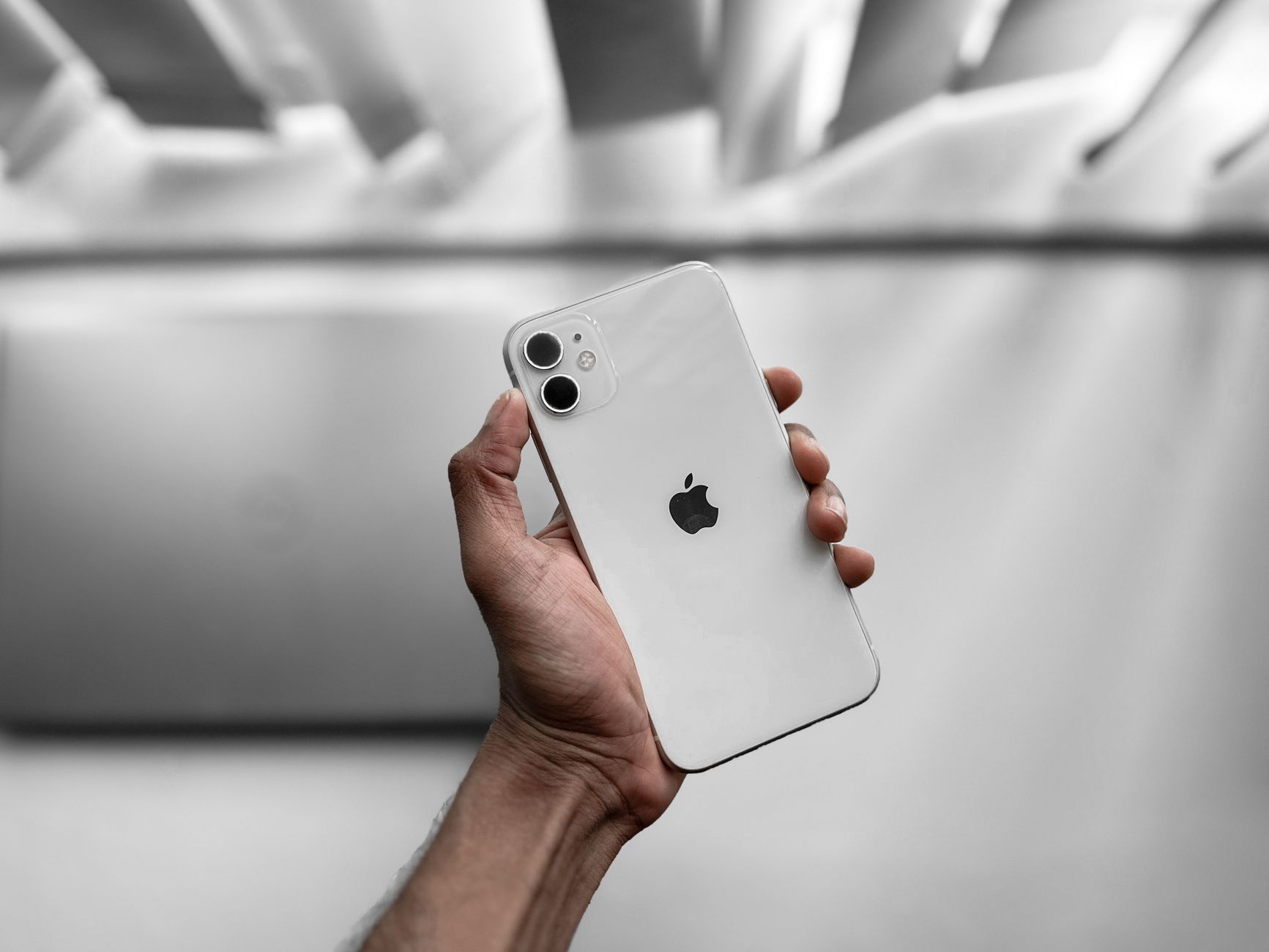 A close-up image of a hand holding a white smartphone indoors with a blurred background.