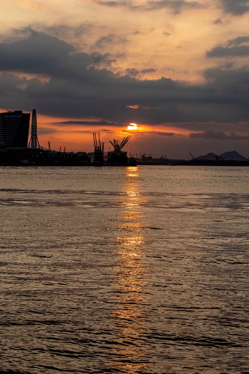 Free Beautiful sunset at Rio de Janeiro's waterfront with silhouetted cranes and city skyline. Stock Photo