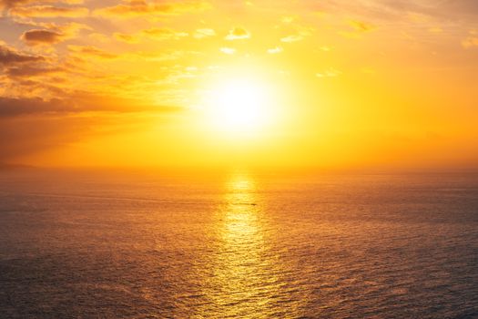 Dramatic golden sunset with vibrant skies reflecting over a calm ocean horizon.