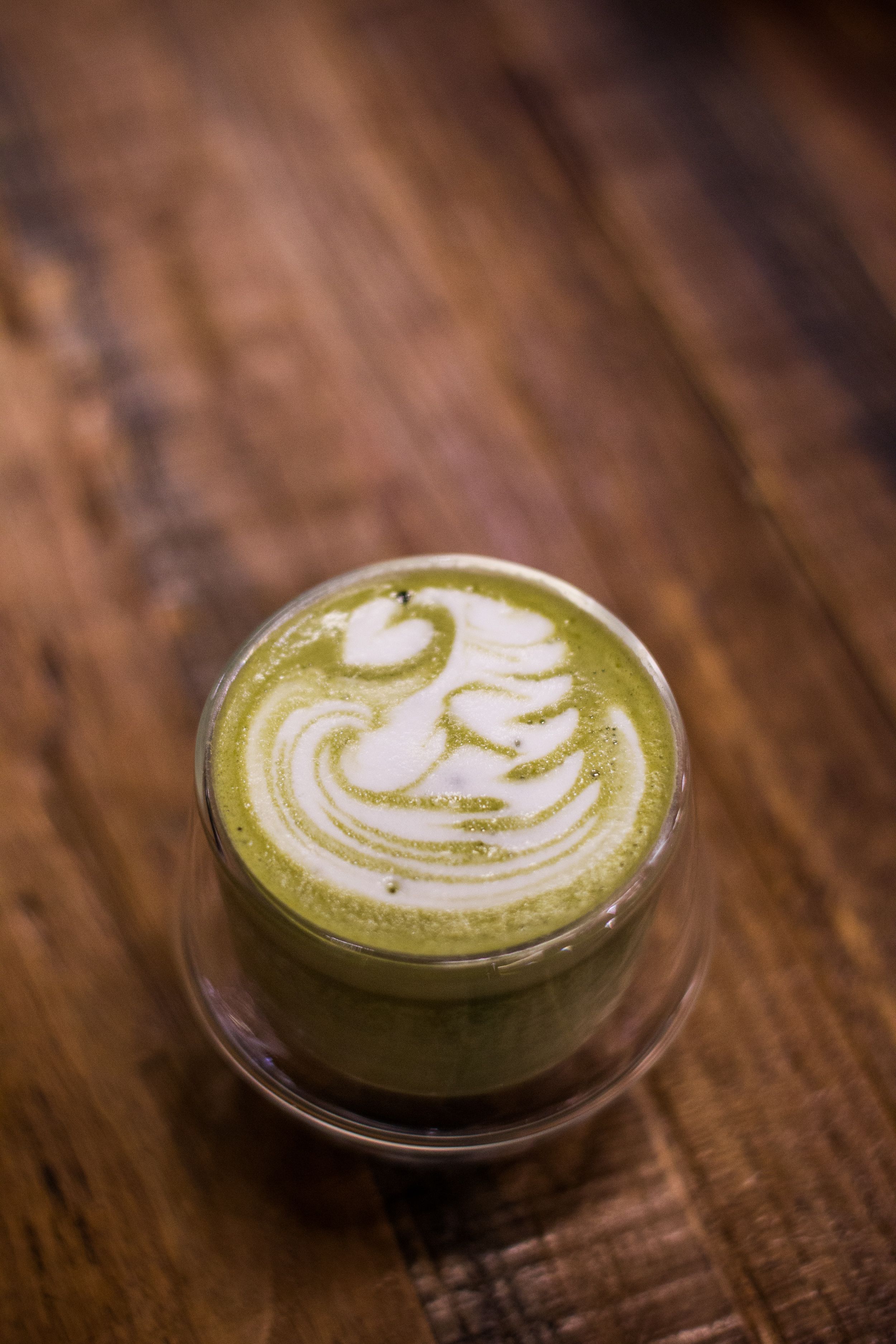 Finished green latte with white foam art in a clear glass cup
