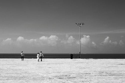 Black and White Photo of People Walking on a Beach 