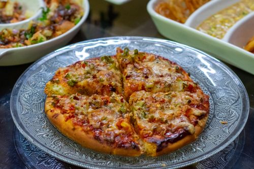 Free Delicious homemade veggie pizza with cheese and toppings on decorative glass plate. Stock Photo