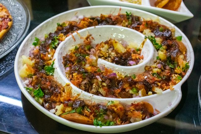 A vibrant and colorful spiral platter of Indian Aloo Chaat garnished with herbs.