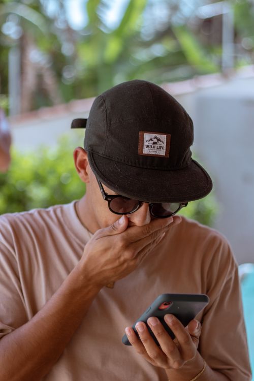 Free Adult man with cap and sunglasses using smartphone outdoors in Guarapari, Brazil. Stock Photo
