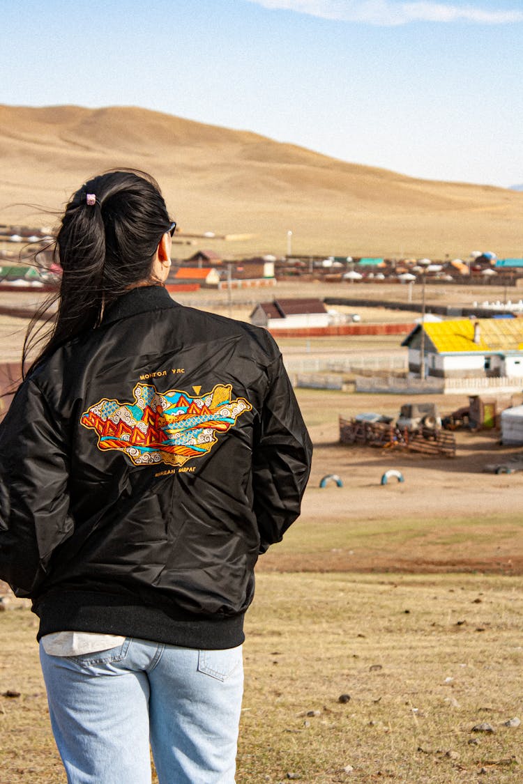 Woman In A Black Jacket And Jeans Looking At A Village In A Desert 