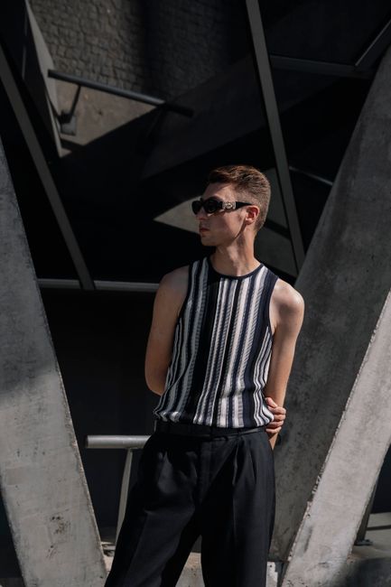 Stylish young man posing in stripes outdoors, wearing sunglasses against a modern architectural backdrop.