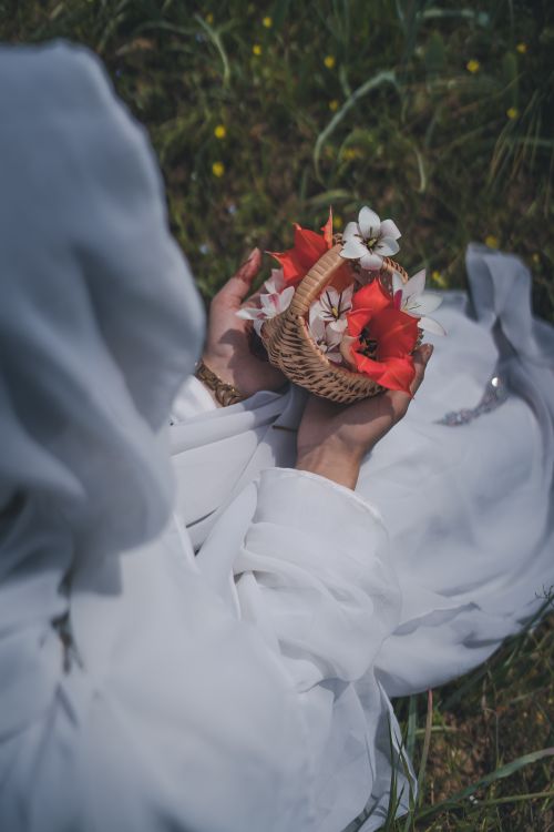 Free A woman in white clothing holding a basket with vibrant flowers, captured outdoors on grass. Stock Photo