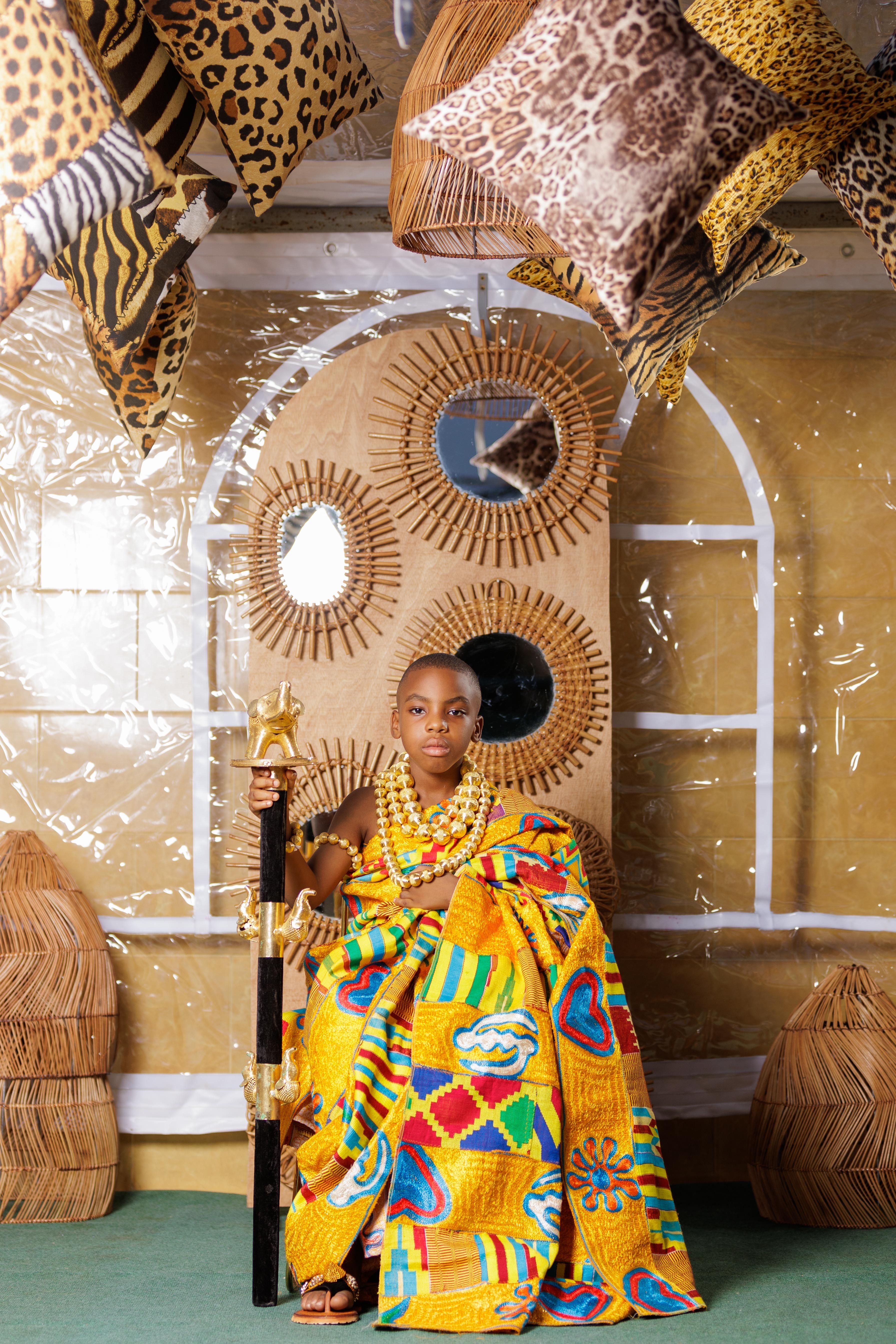 Vibrant portrait of a young African child in traditional attire sitting indoors with cultural decorations.