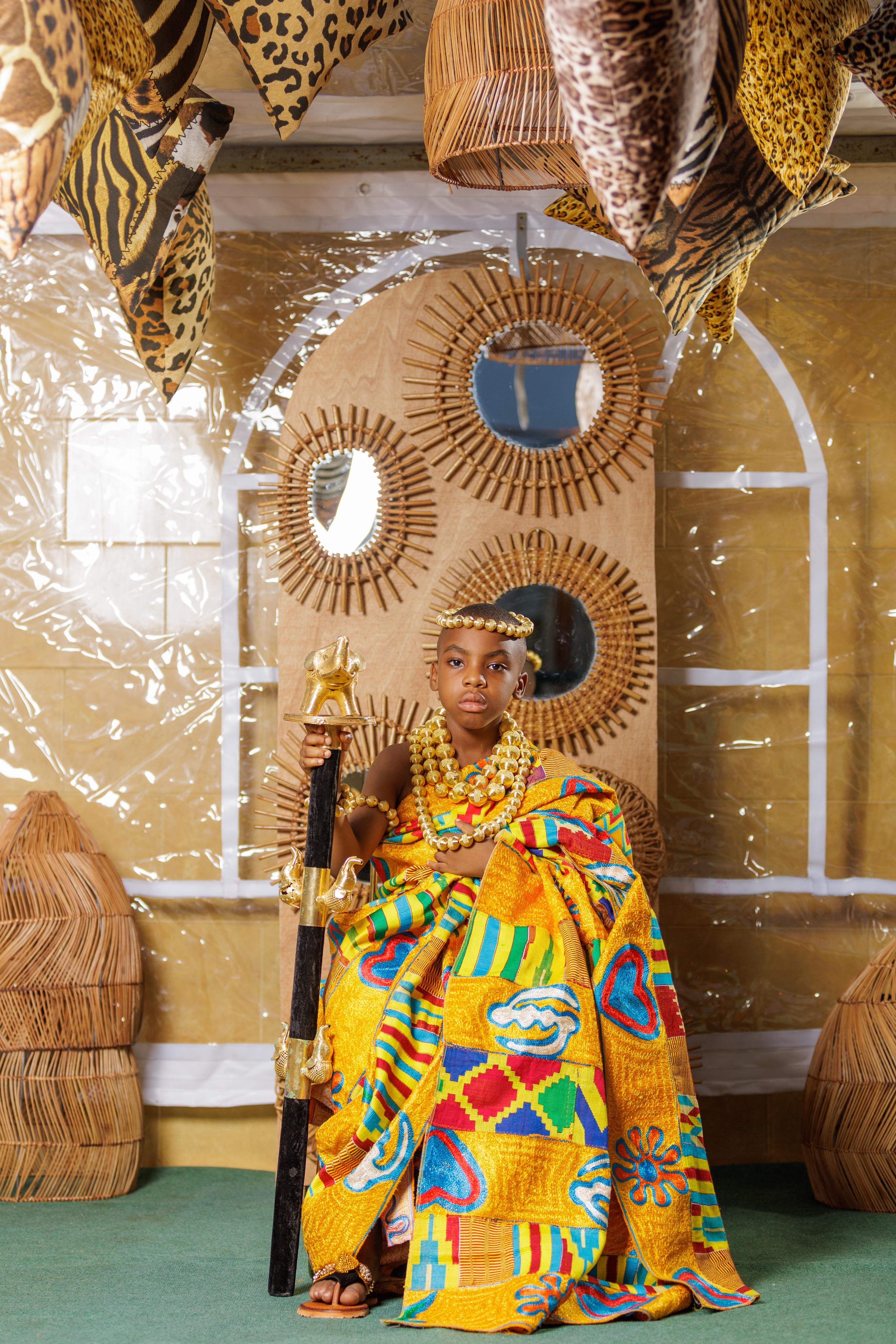 African boy seated in vibrant traditional attire, showcasing rich cultural heritage indoors.