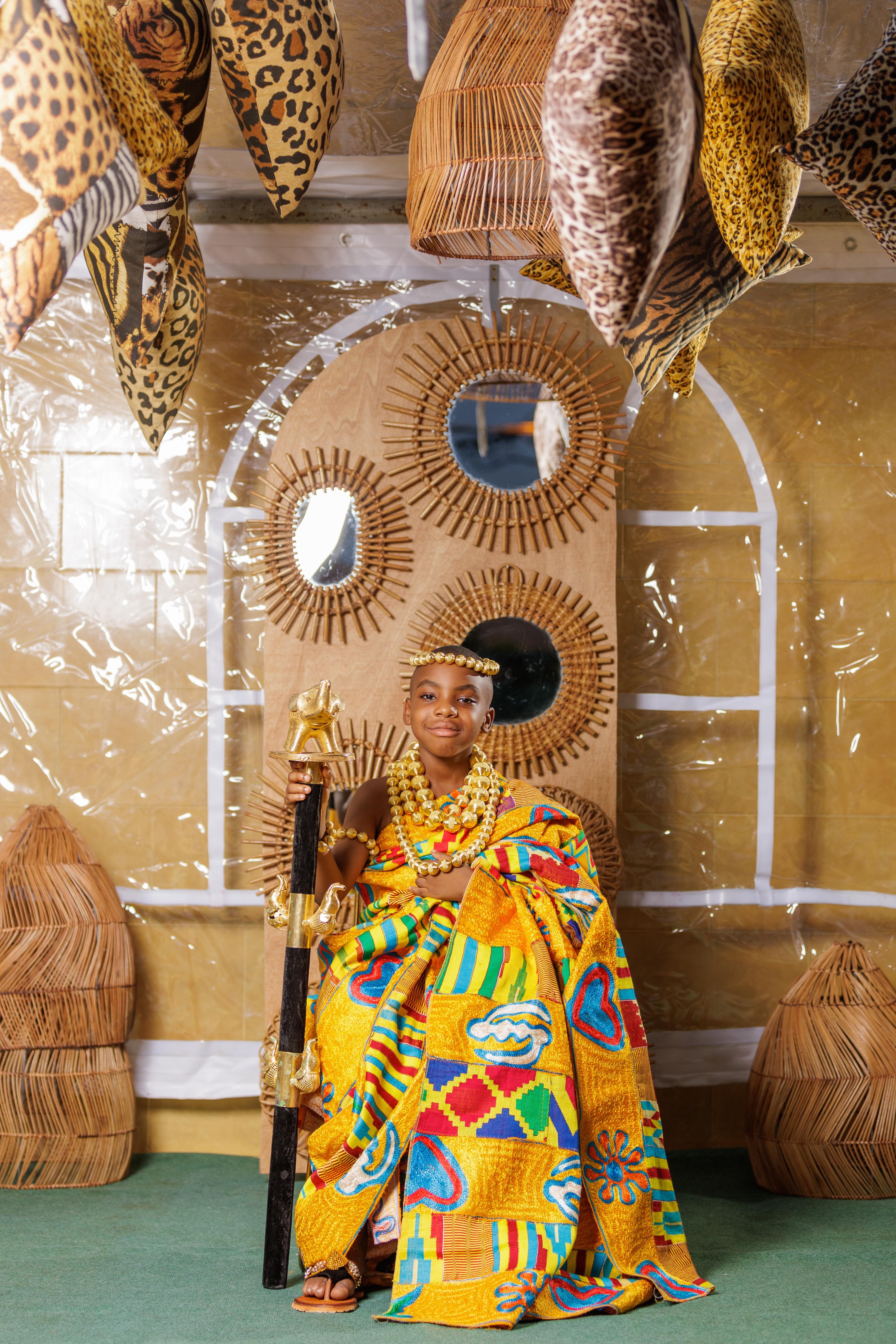 A vibrant portrait capturing an African child dressed in traditional attire with intricate patterns, seated in an artistic setting.