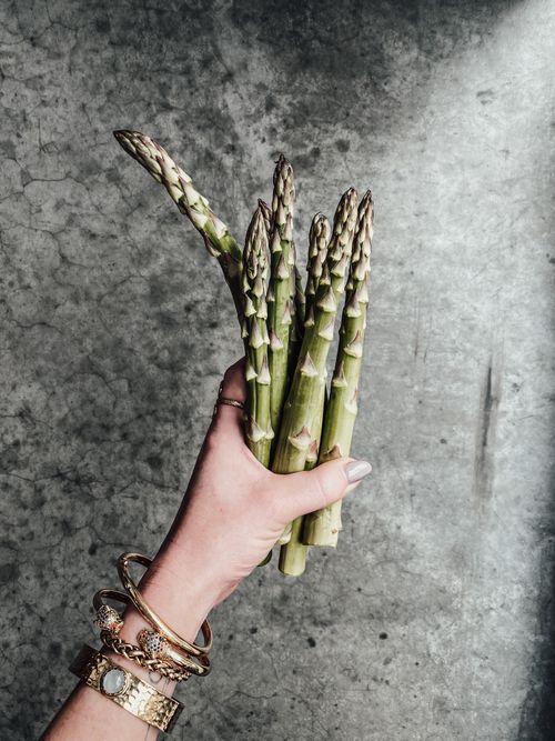 Free Close-up of a woman's hand holding fresh asparagus against a gray background. Stock Photo