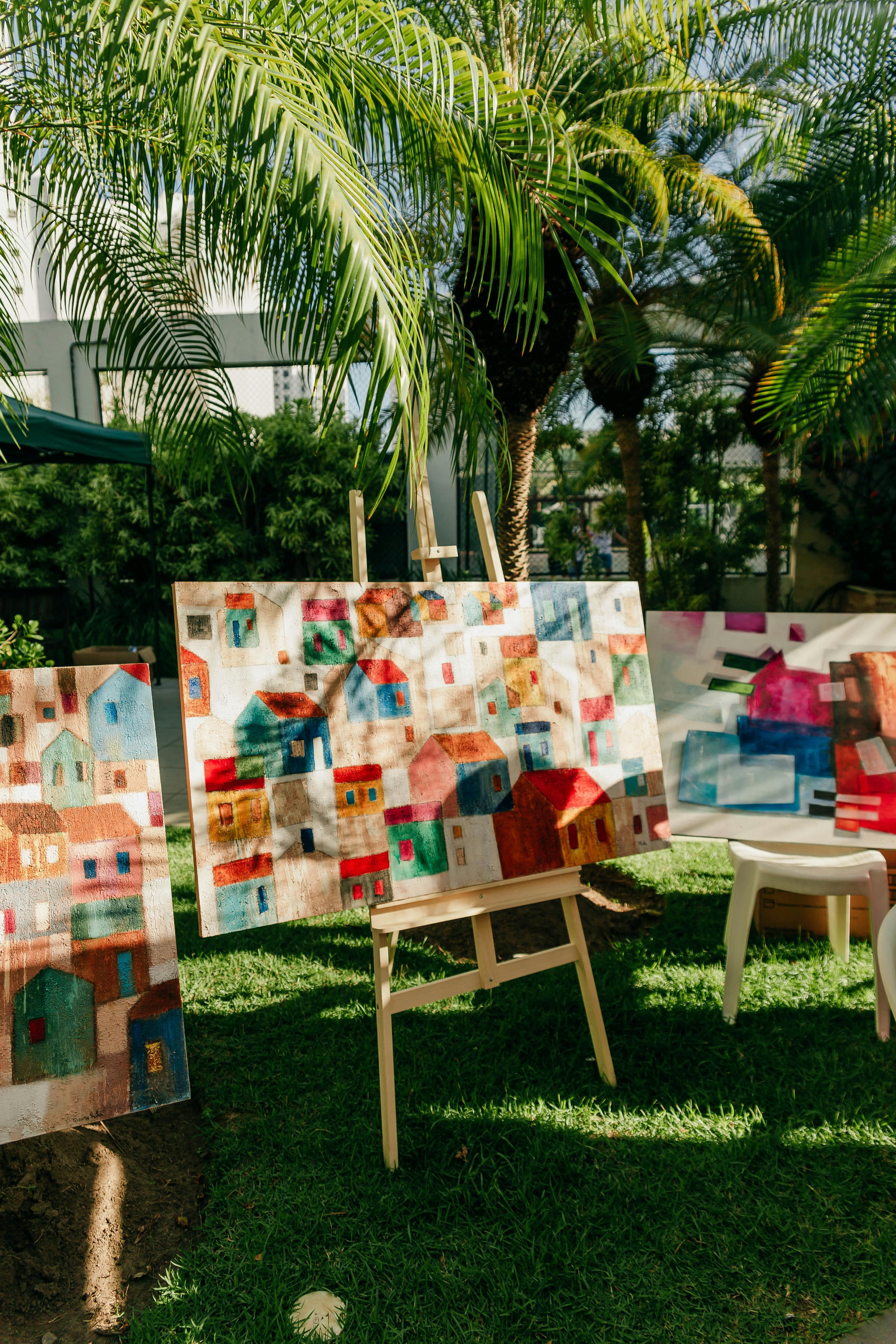 Vibrant paintings of abstract houses displayed in a sunny garden setting.