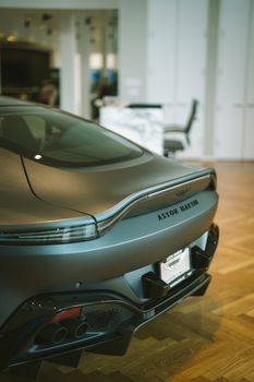 Gray Aston Martin Vantage displayed in a sleek indoor showroom, showcasing its elegant design from the rear view.
