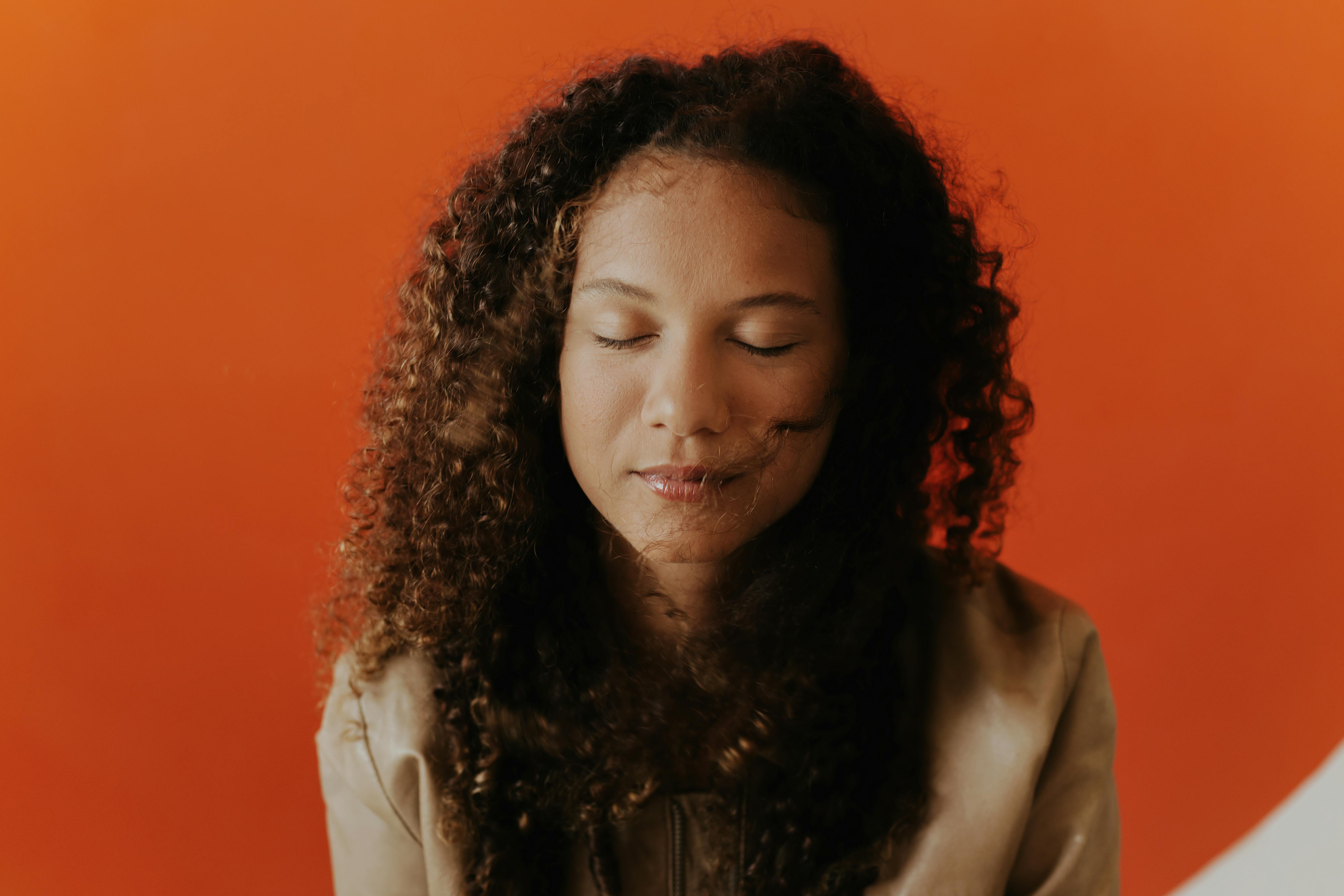 Portrait of a woman with curly hair and eyes closed against a vibrant red background.