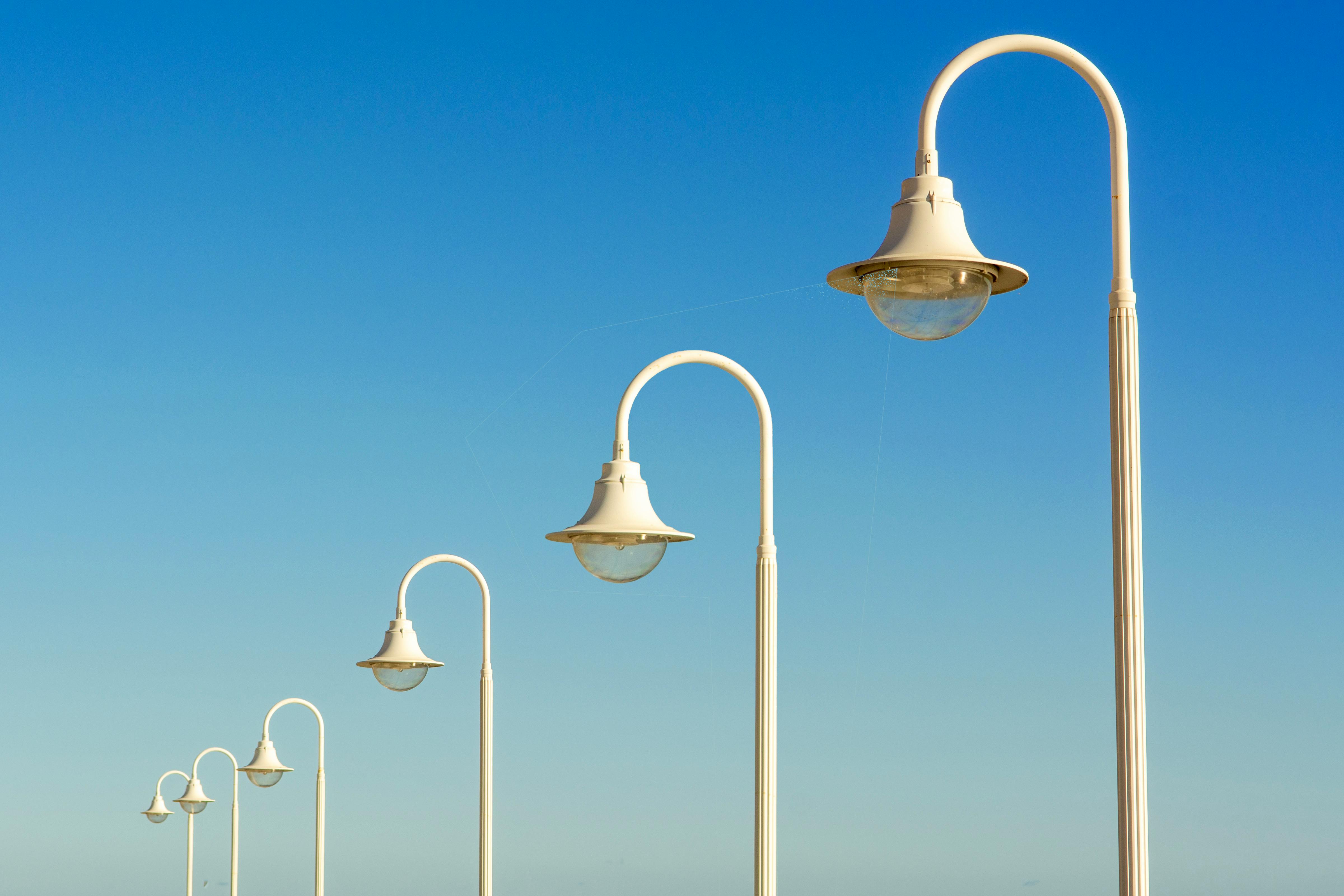 White street lamps line up with diminishing perspective under a clear sky, creating a sleek and modern urban scene.