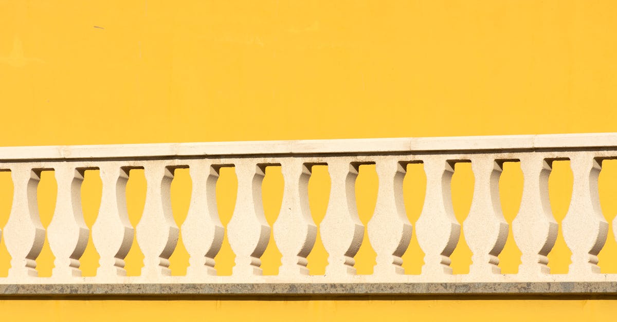 Minimalist photo of a white railing in front of a vibrant yellow wall, showcasing architectural detail.
