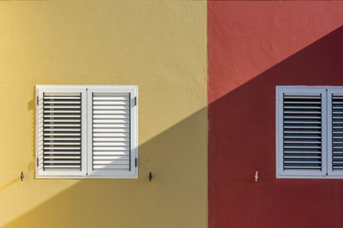 Free Colorful urban facade with yellow and red walls featuring white shuttered windows in bright daylight. Stock Photo