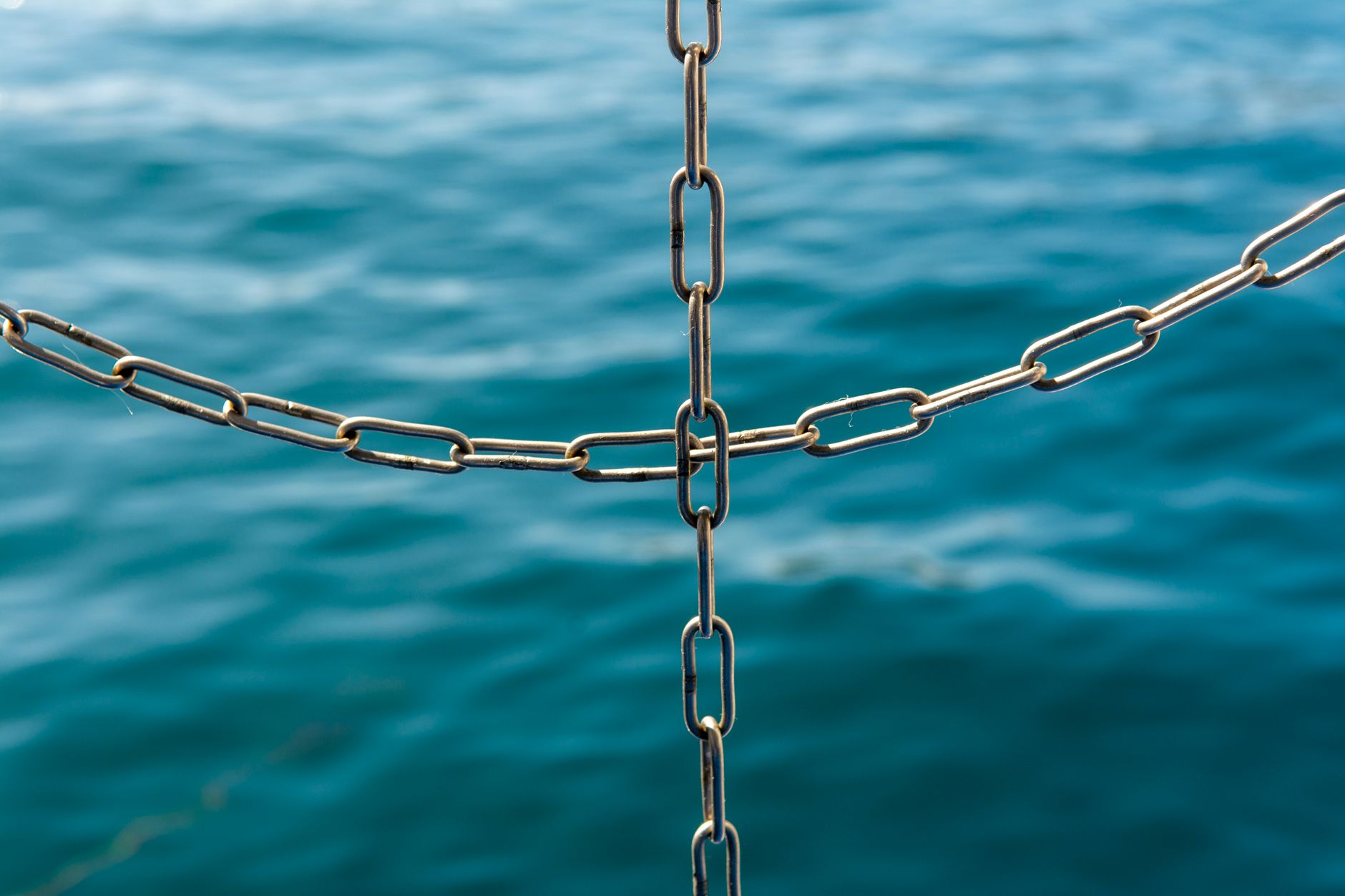 Close-up of interconnected metal chains with the ocean blurred in the background.