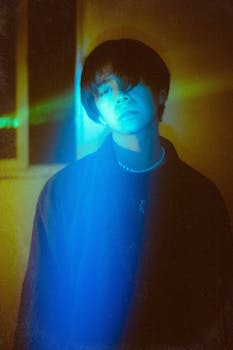 Moody artistic portrait with vibrant blue and green lighting effects.