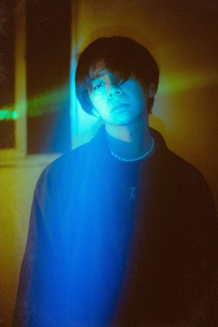 Moody artistic portrait with vibrant blue and green lighting effects.