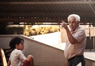 一位老人和一个小男孩在户外树冠下打手势交谈