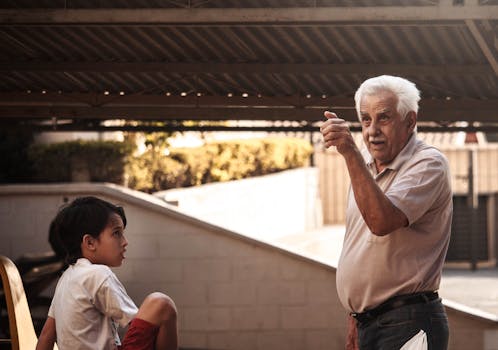 一位老人和一个小男孩在户外树冠下打手势交谈